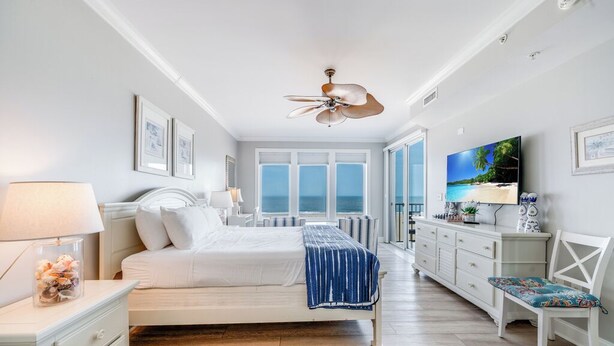 Un dormitorio con cama, mesita de noche, cómoda, televisor y vista al mar.
