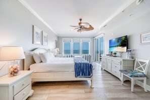 Un dormitorio con cama, mesita de noche, cómoda, televisor y vista al mar.