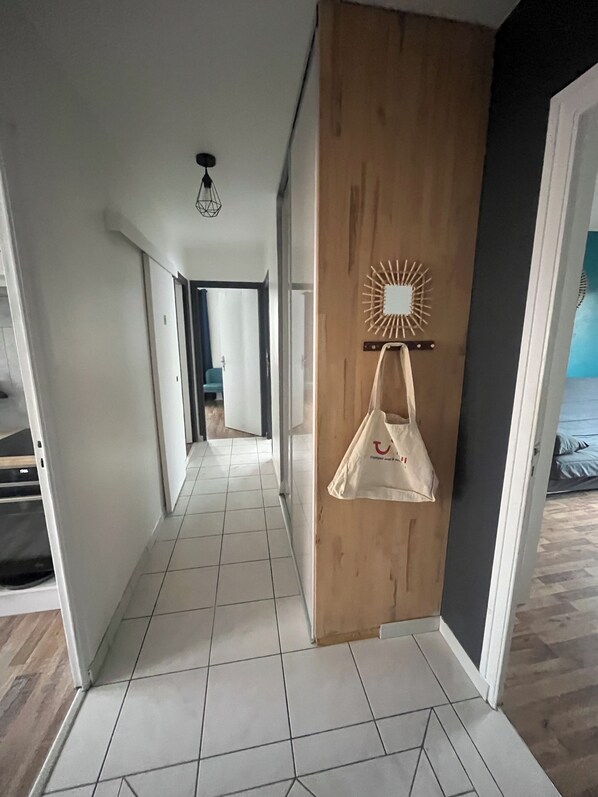 A hallway with a wooden door, a hanging bag, and a sunburst wall decoration.