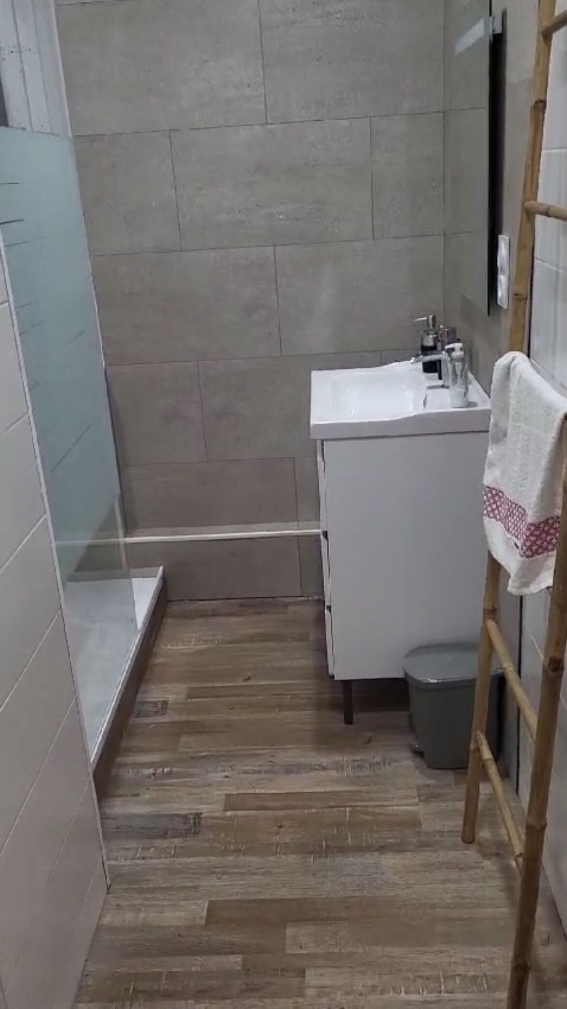 A small bathroom with a wooden floor, a white sink, and a towel hanging on a rack.