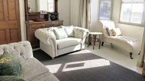 A traditional living room with a large wooden dresser, a tufted sofa, a smaller armchair, and a round table. - Short breaks available!! (St Davids)