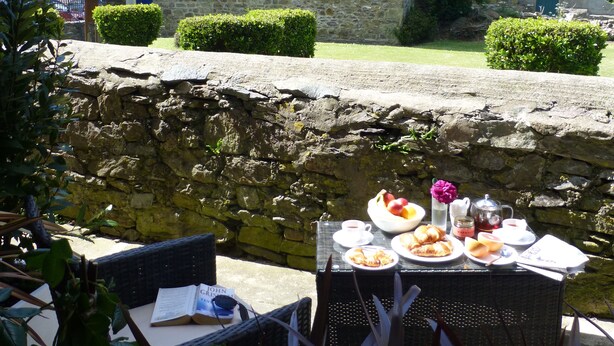 A stone building with a pitched roof and a chimney. In front of the building, there is a stone wall and a small table with plates of food, a cup, and a flower. - Short breaks available!! (St Davids)