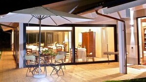 An outdoor dining area with a covered patio, glass doors leading to a dining room, and a view of the night sky.