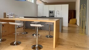 A modern kitchen with a central island, bar stools, pendant lights, and a view of the living area.