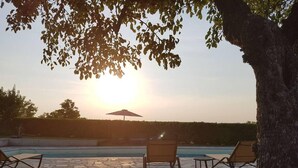 A poolside area with lounge chairs and an umbrella, surrounded by trees and a clear sky.