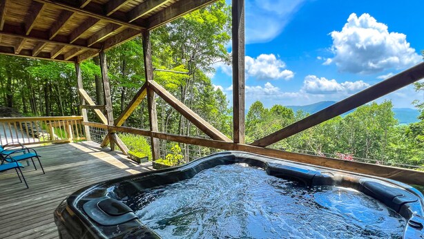 A hot tub under a wooden deck with a view of a forest and mountains. - El Cabitan: 4BR Scenic Mountain Views, Hot Tub, Game Room & Fire Pit (West Jefferson)