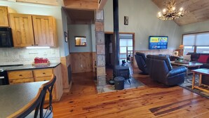 A spacious living area with a wooden floor, a sofa, a coffee table, and a TV mounted on the wall. - El Cabitan: 4BR Scenic Mountain Views, Hot Tub, Game Room & Fire Pit (West Jefferson)
