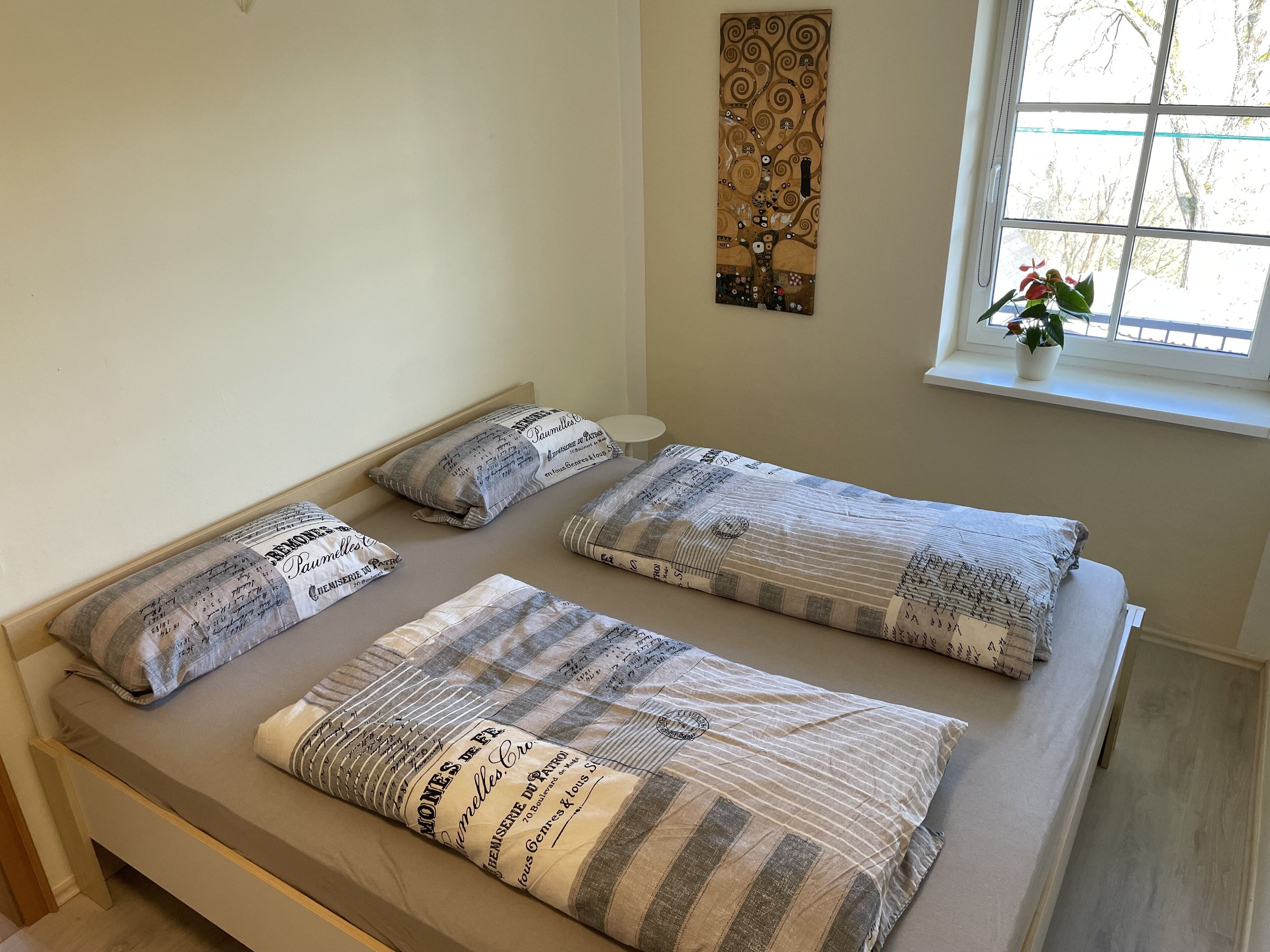 Un lit avec une couverture à rayures et des oreillers, une fenêtre avec une plante et un élément décoratif sur le mur.