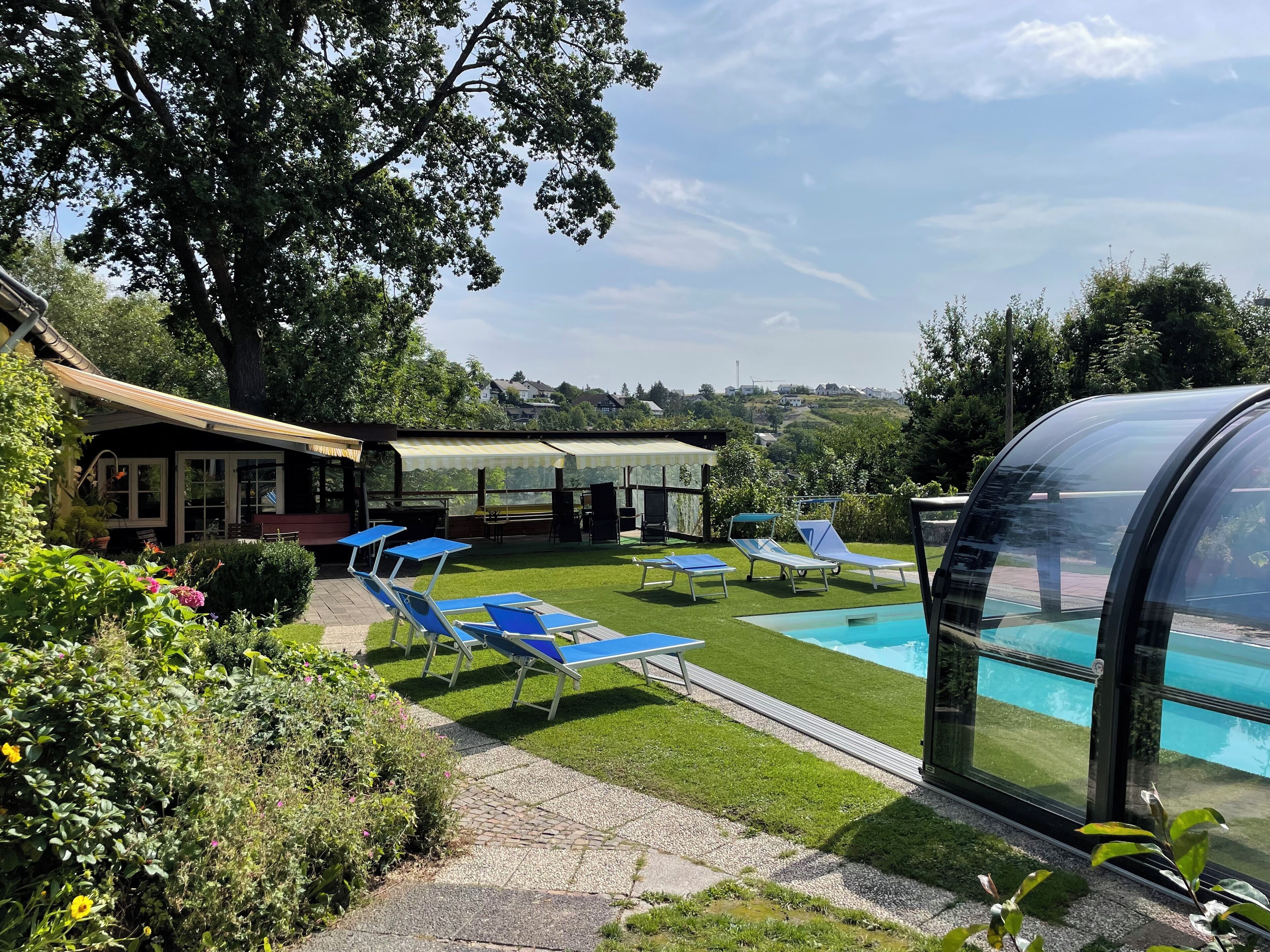 Un espace piscine doté de chaises longues, d’un coin salon abrité et offrant une vue sur le paysage environnant.