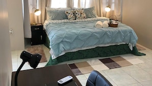 Ein ordentlich eingerichtetes Schlafzimmer mit Bett, Nachttischlampen, Nachttisch, Sessel und kleinem Tisch mit Fernbedienung.