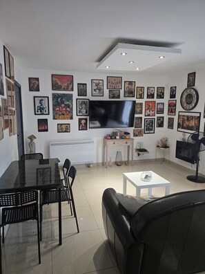 Ein modernes Wohnzimmer mit einem Flachbildfernseher, einem Esstisch mit Stühlen, einer Couch und verschiedenen gerahmten Kunstwerken an den Wänden.