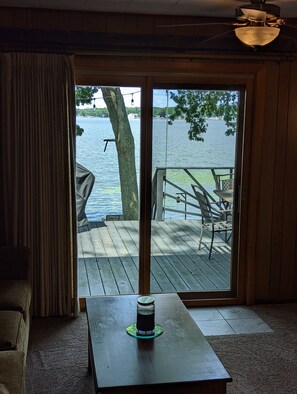 Una habitación con vistas a un lago a través de un ventanal corredero, una terraza de madera en el exterior y una mesa con una vela.