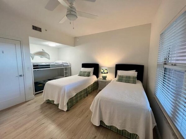 A bedroom with two beds, a ceiling fan, a window with blinds, and a wardrobe.