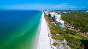 An aerial view of a coastal area with a beach, buildings, and a road.