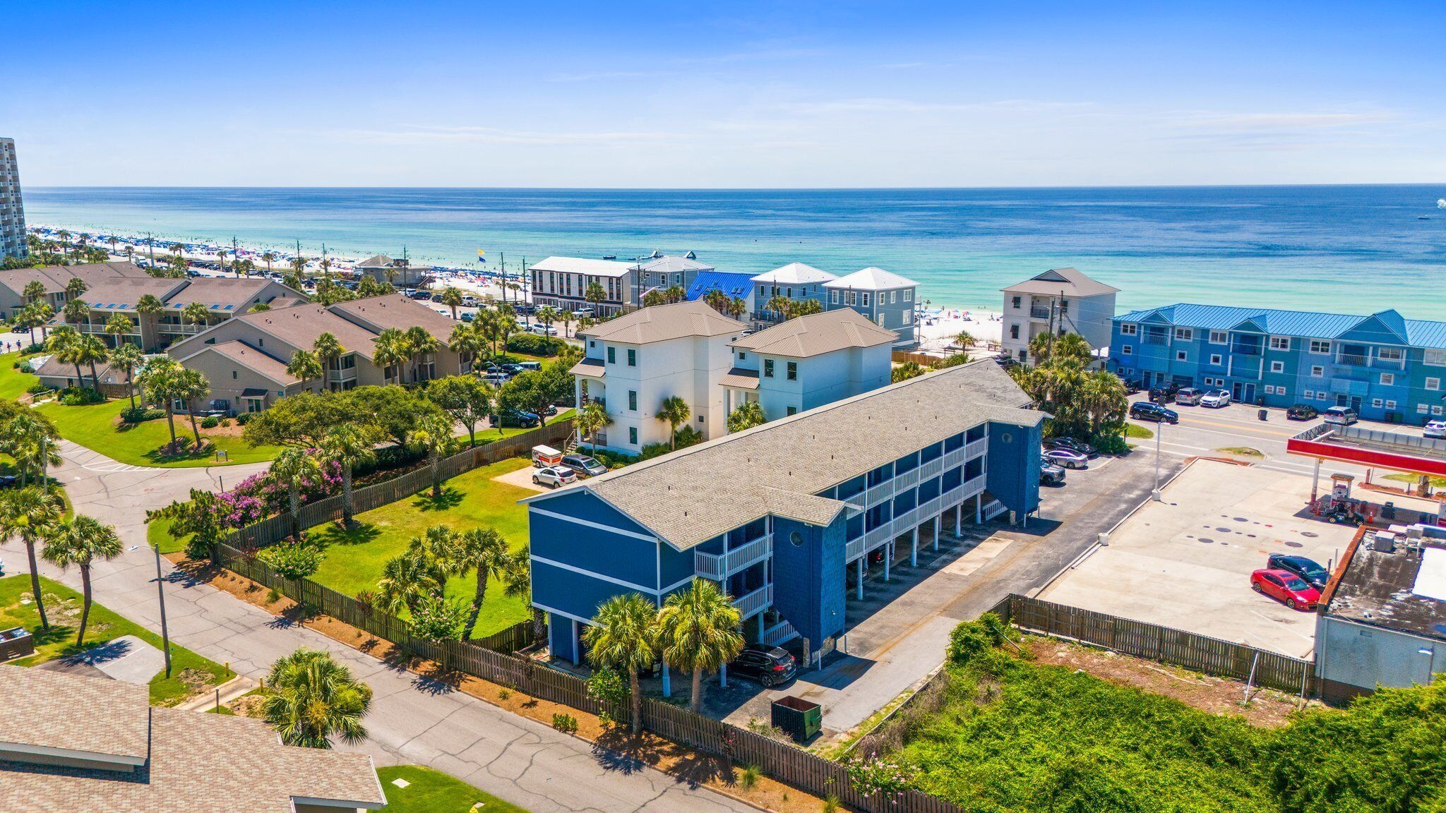 A coastal hotel with multiple buildings, a parking lot, and a beach in the background.
