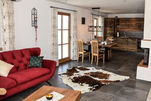 A modern living room with a red sofa, wooden dining table, and a kitchen with dark wood cabinets.