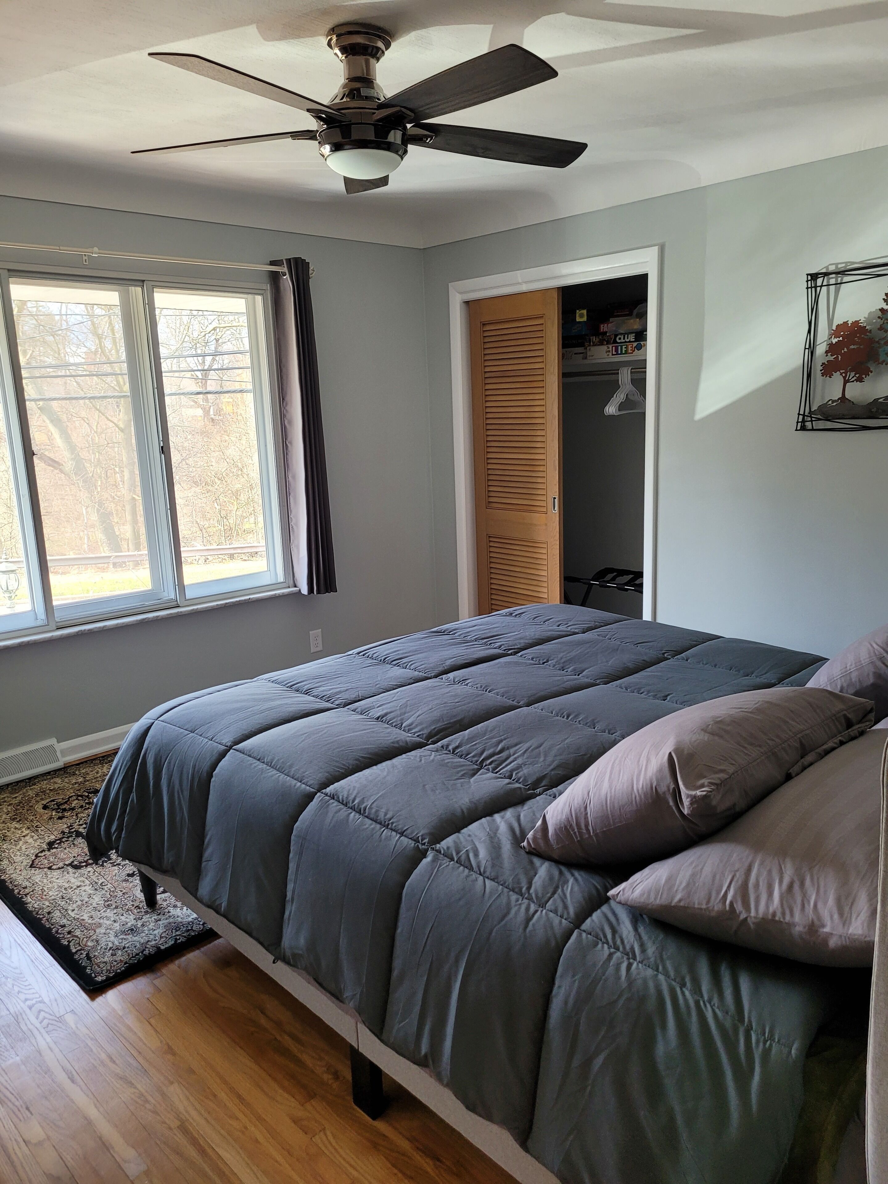 Une chambre à coucher comprenant un lit, un ventilateur de plafond, une fenêtre et une porte donnant sur un placard.