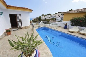 A swimming pool with dolphins, a potted plant, and a view of the sea.