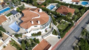 An aerial view of a residential area with a curved-roofed house, a swimming pool, and a road.
