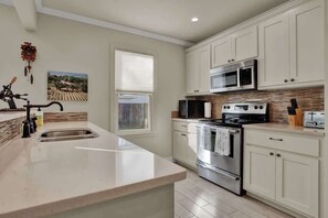 A kitchen with white cabinets, stainless steel appliances, and a large island with a sink. - Hot Tub + Fire Pit | Wine Country | Near Main St (Fredericksburg)