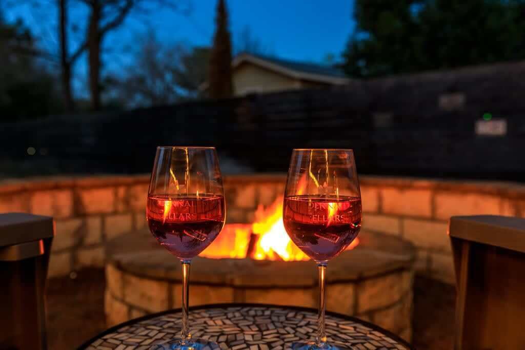 Two glasses of red wine on a table with a fire pit in the background.