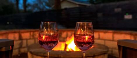 Two glasses of red wine on a table with a fire pit in the background.