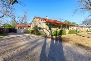 A two-story house with a garage, a covered porch, and a gravel driveway. - Hot Tub + Fire Pit | Wine Country | Near Main St (Fredericksburg)