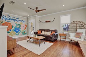A living room with a brown leather sofa, a wooden coffee table, a white armchair, and a colorful floral wall mural.