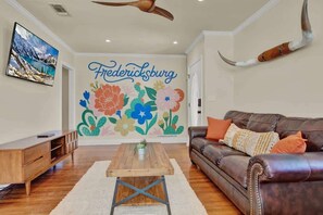 A living room with a brown leather sofa, a wooden coffee table, and a wall mural with the word 'Fredericksburg' and floral designs.