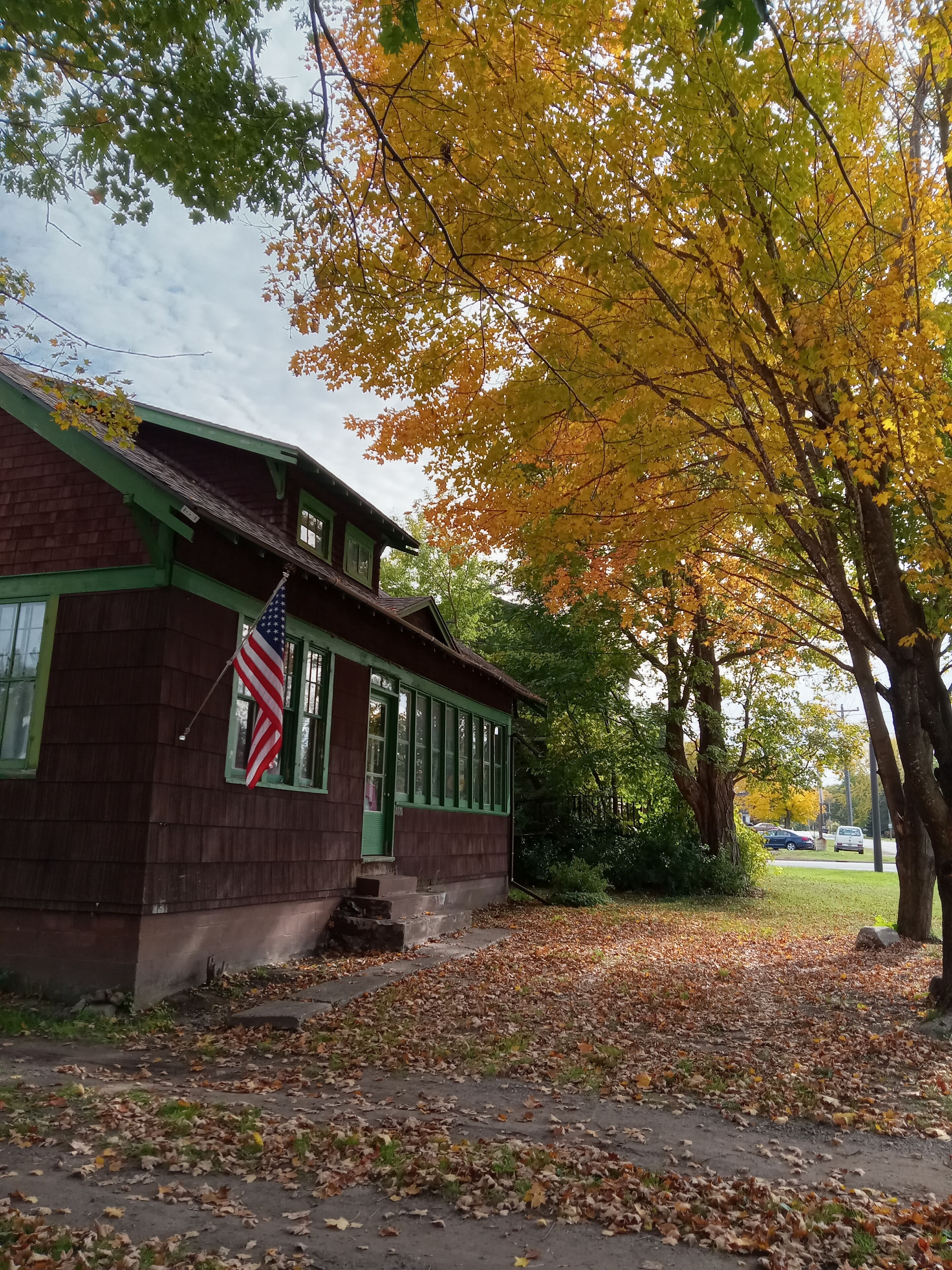 A building with a green roof and an American flag, surrounded by trees with yellow leaves.
