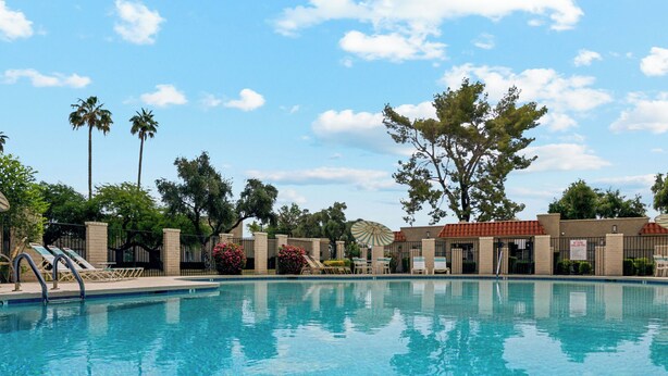 A clear swimming pool with a view of a building with a red roof and palm trees in the background. - Wonderful 3 bedroom/2 bath, close to everything! (Scottsdale)
