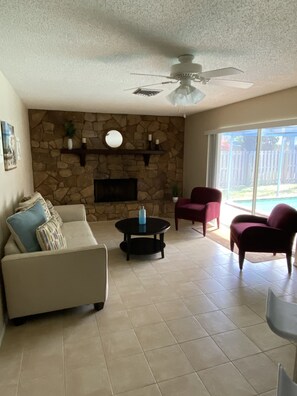 Relax in this inviting living room with a fireplace, flat-screen TV, and comfortable seating area leading to an outdoor space with a pool.
