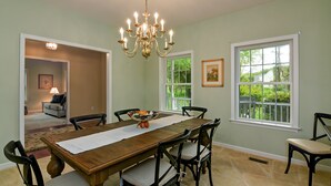 A dining room with a wooden table, chairs, a chandelier, and large windows. - Tranquil  Beautiful Waterfront  Near Historic St. Michaels & Royal Oak (easton)