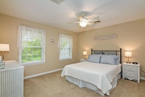 A bedroom with a bed, two bedside tables with lamps, a ceiling fan, and two windows with curtains.