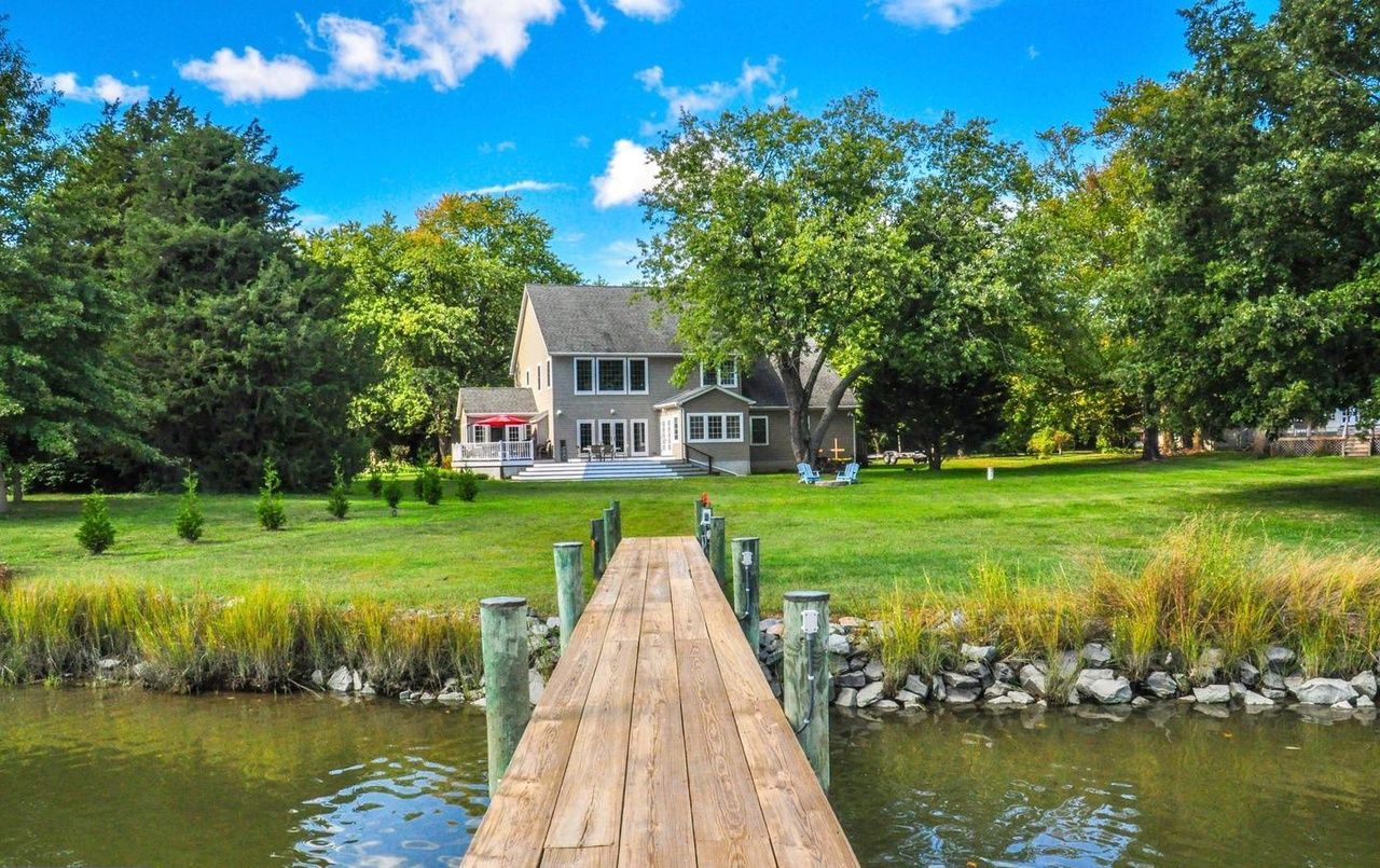 A house with a dock leading to a pond, surrounded by trees and a well-maintained lawn.