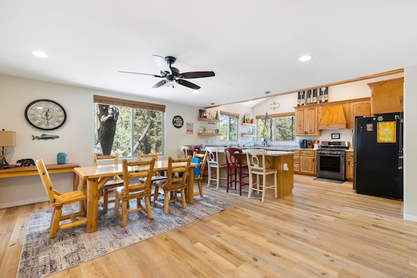 Une cuisine moderne avec des meubles en bois, un réfrigérateur noir et un coin repas comprenant une table et des chaises en bois.