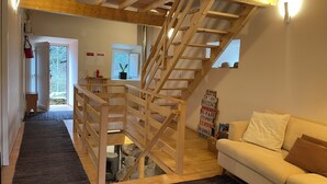 A wooden staircase leading to an upper level, a cozy living area with a sofa, and a small kitchen area with a window. - Unique Experience in the Heart of Nature (Chãos)