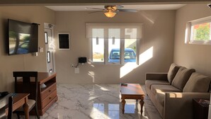 A living room with a ceiling fan, a TV mounted on the wall, a sofa, a coffee table, and a TV stand. - Aruba 2-bedroom duplex for rent. 4 minutes to Eagle Beach and close to shopping. (Noord)