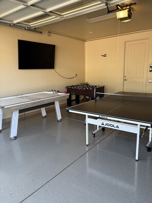 A ping pong table with a net, a foosball table, and a television mounted on the wall. - Desert Tranquility 4 Bedroom with Heated Pool (Scottsdale)