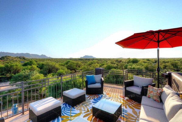 A terrace with wicker furniture, a red umbrella, and a view of green hills. - Desert Tranquility 4 Bedroom with Heated Pool (Scottsdale)