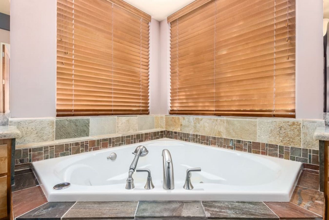 A bathroom with a freestanding bathtub, wooden blinds, and a tiled backsplash.