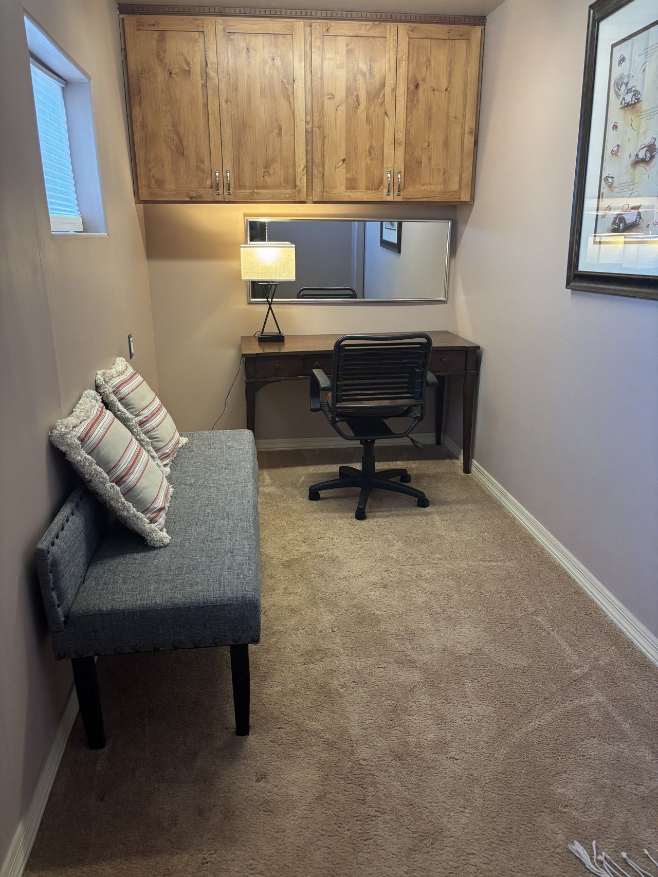A small, carpeted room with a desk, chair, and a cushioned bench.