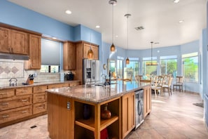 A spacious kitchen with wooden cabinets, a large island, and a dining area with chairs and a table. - Desert Tranquility 4 Bedroom with Heated Pool (Scottsdale)