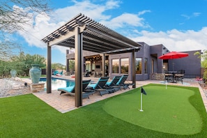A modern house with a covered patio, a swimming pool, and a well-maintained lawn. - Desert Tranquility 4 Bedroom with Heated Pool (Scottsdale)