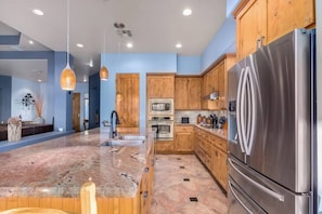 A modern kitchen with granite countertops, stainless steel appliances, wooden cabinets, and pendant lighting. - Desert Tranquility 4 Bedroom with Heated Pool (Scottsdale)