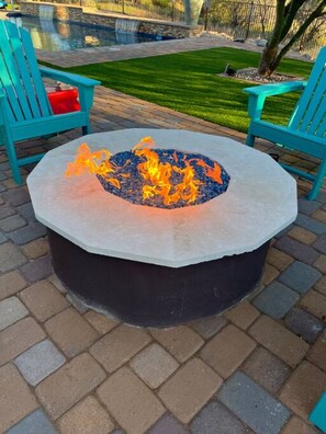 A circular stone fire pit with flames, surrounded by a paved patio with interlocking bricks. - Desert Tranquility 4 Bedroom with Heated Pool (Scottsdale)