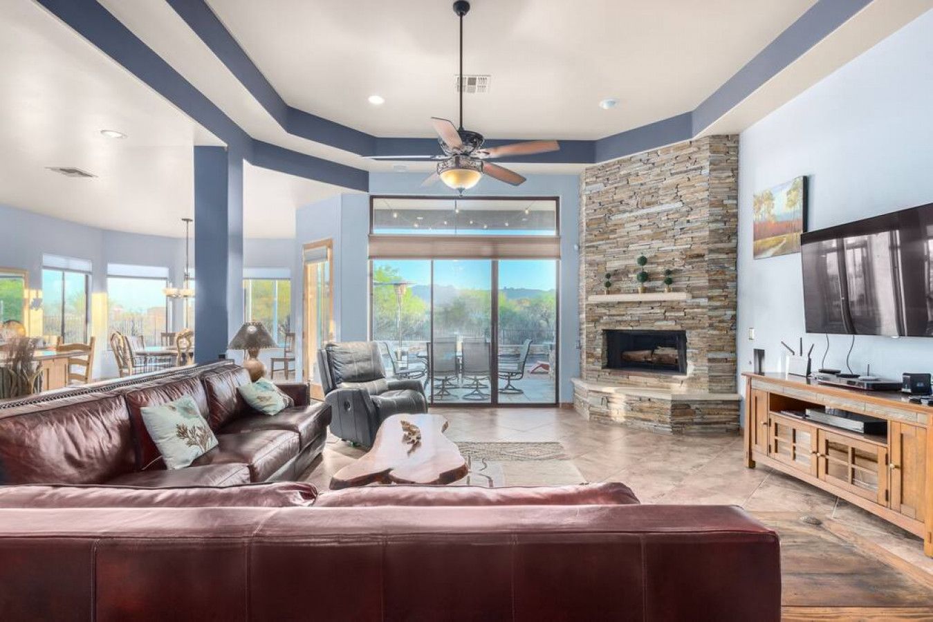 A spacious living room with a leather sofa, a stone fireplace, and a large TV.