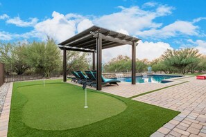 Um quintal com piscina, área de estar coberta e campo de golfe.