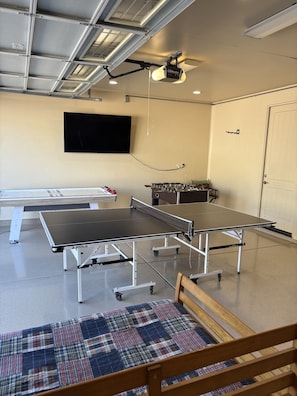 A room with two ping pong tables, a foosball table, a flat-screen TV, and a ceiling fan. - Desert Tranquility 4 Bedroom with Heated Pool (Scottsdale)