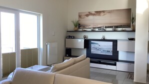 A living room with a large flat-screen TV, a sofa, and a dining area with a table and chairs. - 2 balconies directly by the sea, living room, fireplace, 1 bedroom, kitchen, modern bathroom with shower/WC, washing machine. (Glowe)